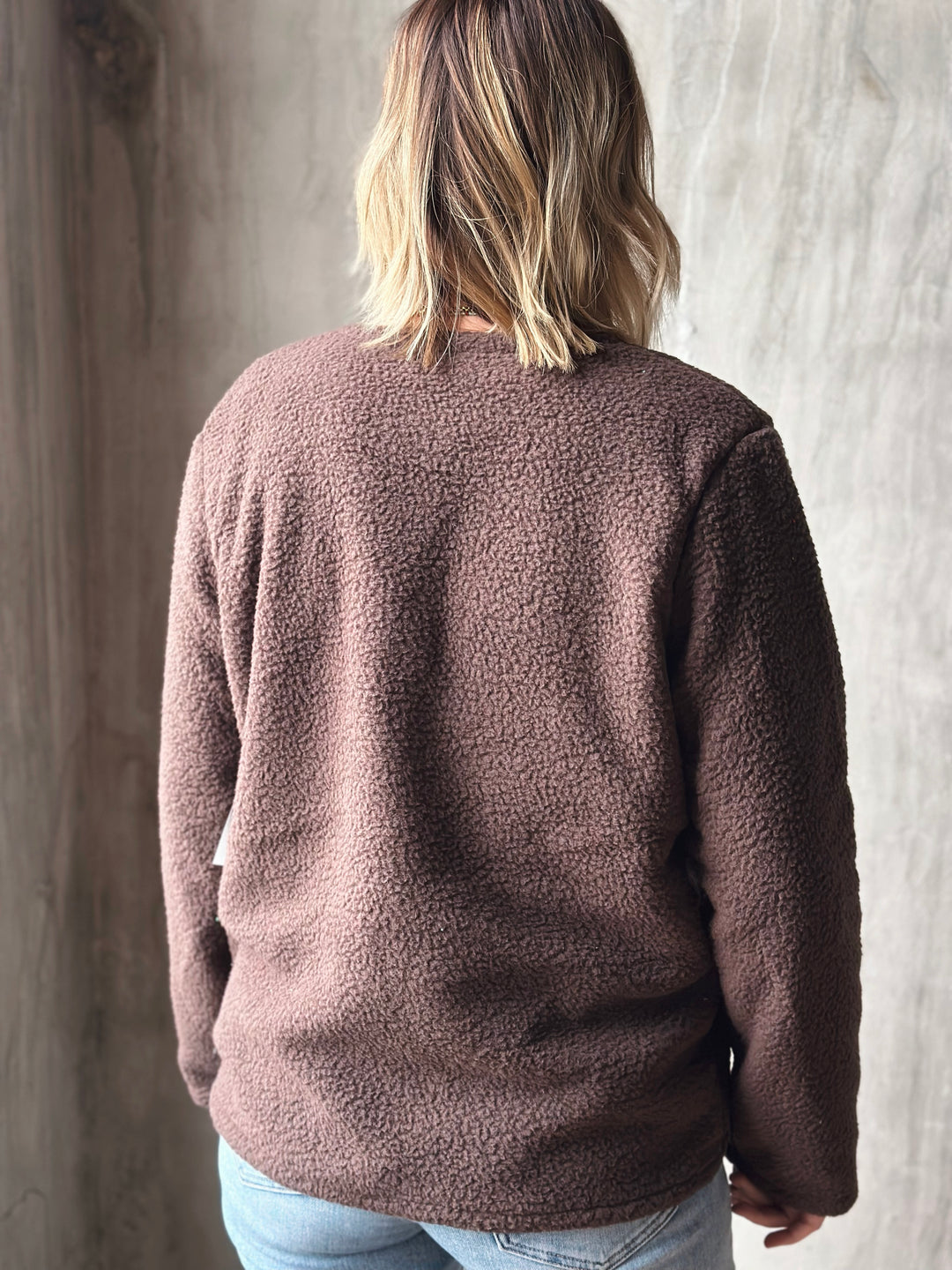Person wearing a brown fleece sweater against a neutral background
