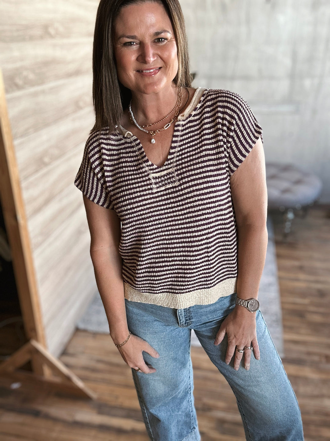 Woman wearing a beige and plum striped v-neck shirt and jeans standing indoors.