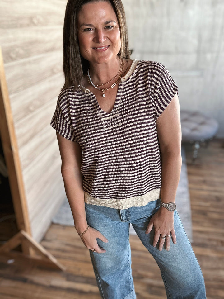 Woman wearing a beige and plum striped v-neck shirt and jeans standing indoors.