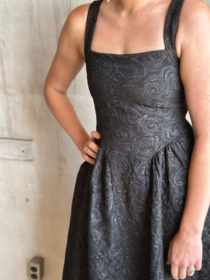 Person wearing a black floral patterned dress against a neutral background