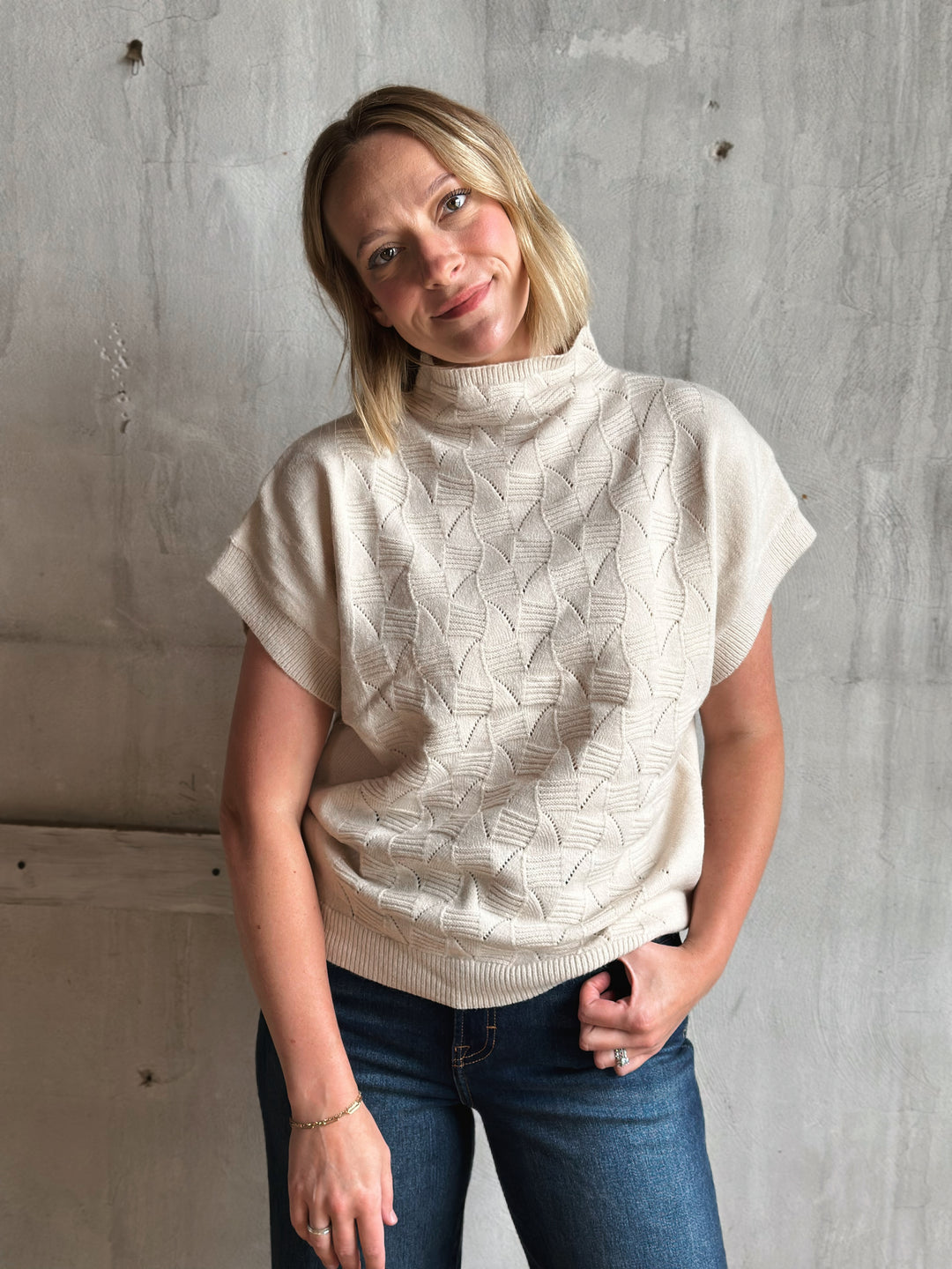 Woman wearing a cream-colored knitted poncho against a gray wall