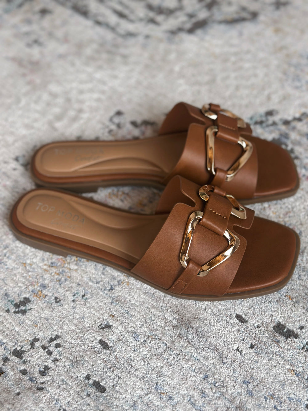 Brown sandals with gold buckles on a textured surface.