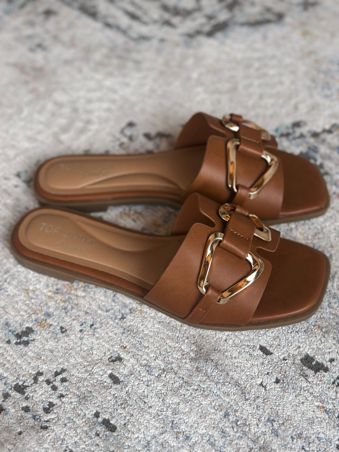 Brown sandals with gold buckles on a textured surface.