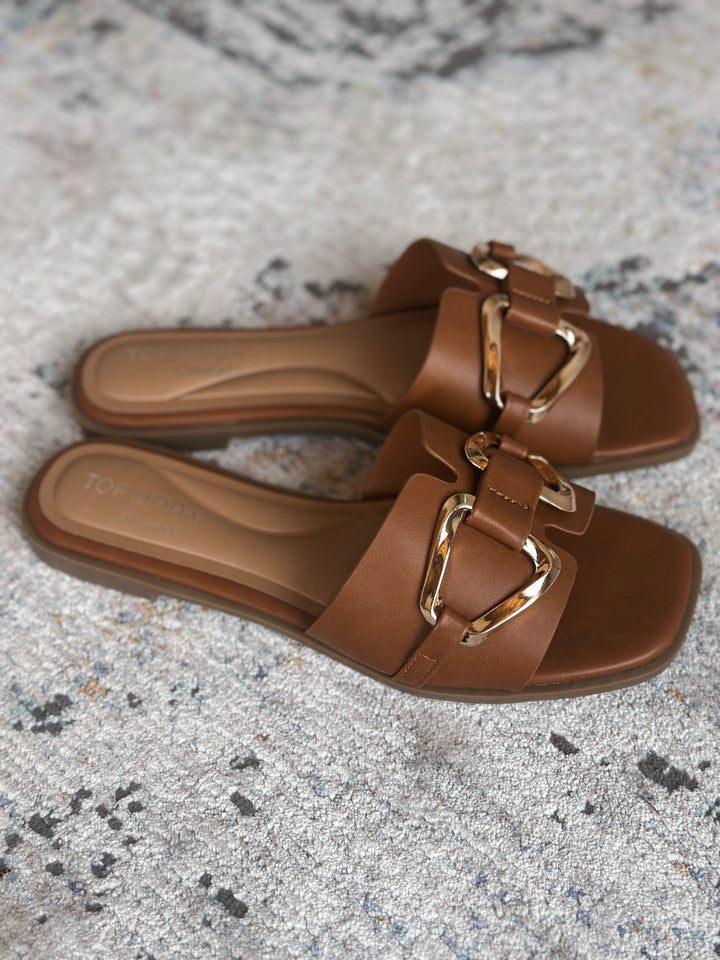 Brown sandals with gold buckles on a textured surface.