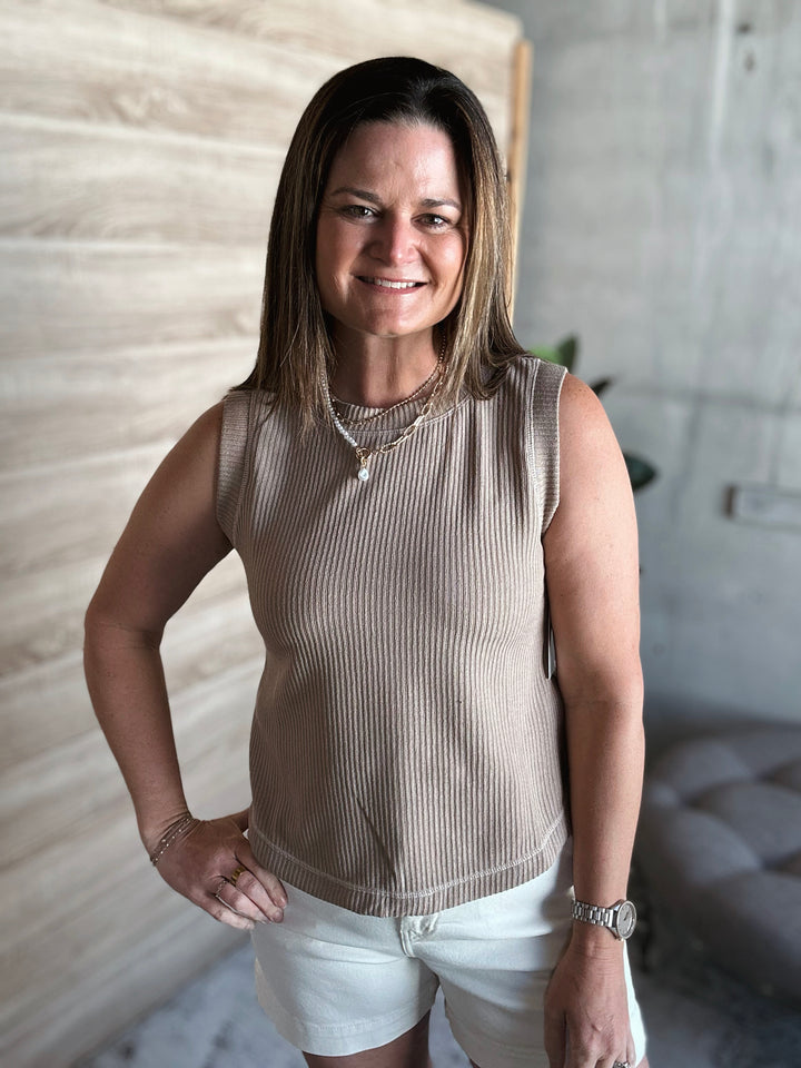 Woman wearing a beige sleeveless top and white shorts standing indoors.