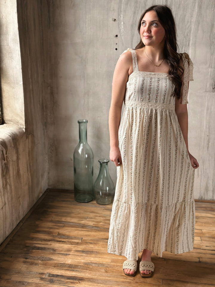 Woman in a long, patterned dress standing in a room with wooden floor and textured walls.