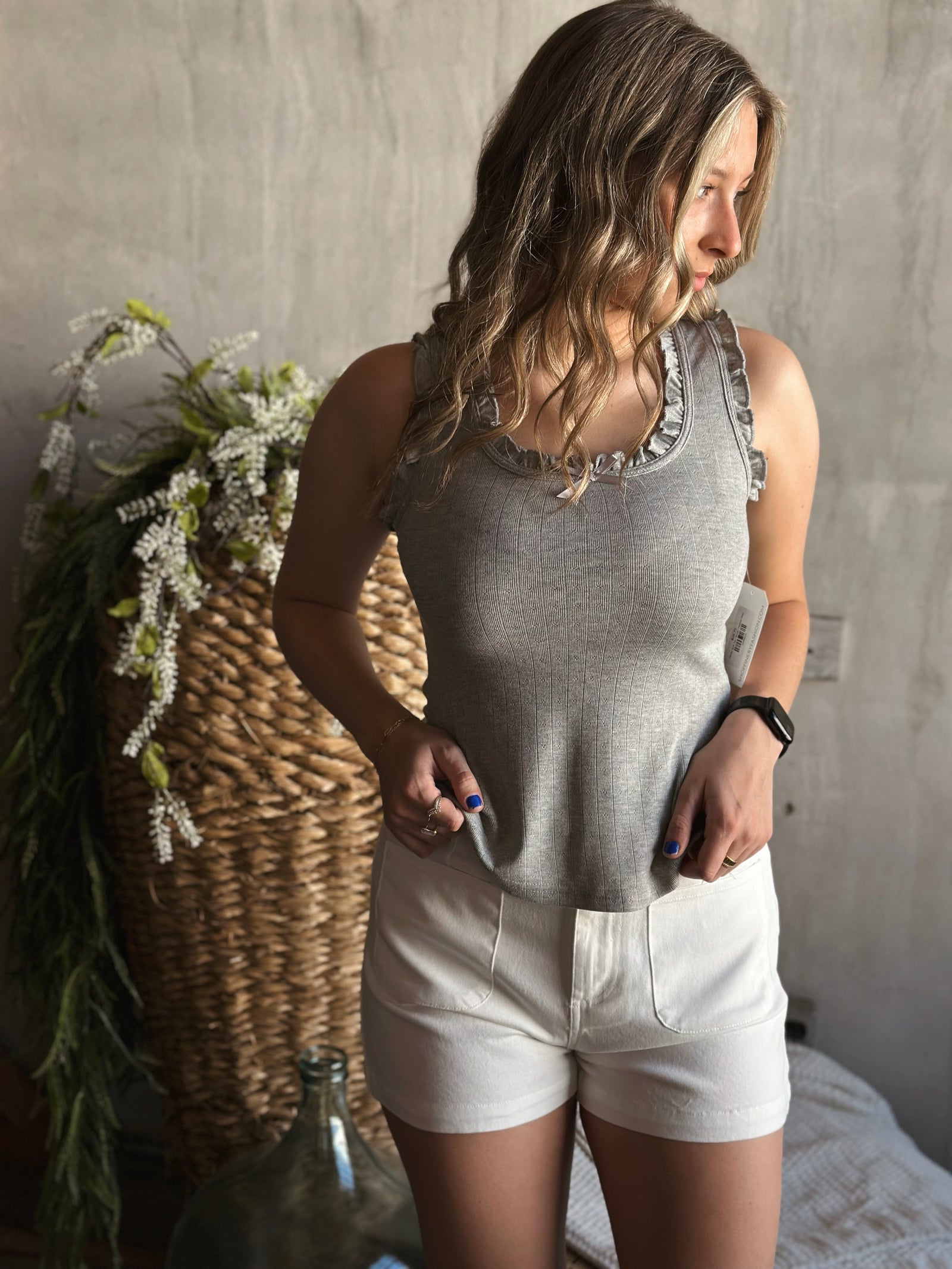 Front view of model wearing a bow trimmed ruffle tank top with a round neckline and a sleeveless design in the color heather 