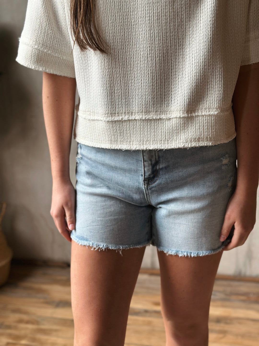 Person wearing a textured white top and light blue denim shorts indoors.