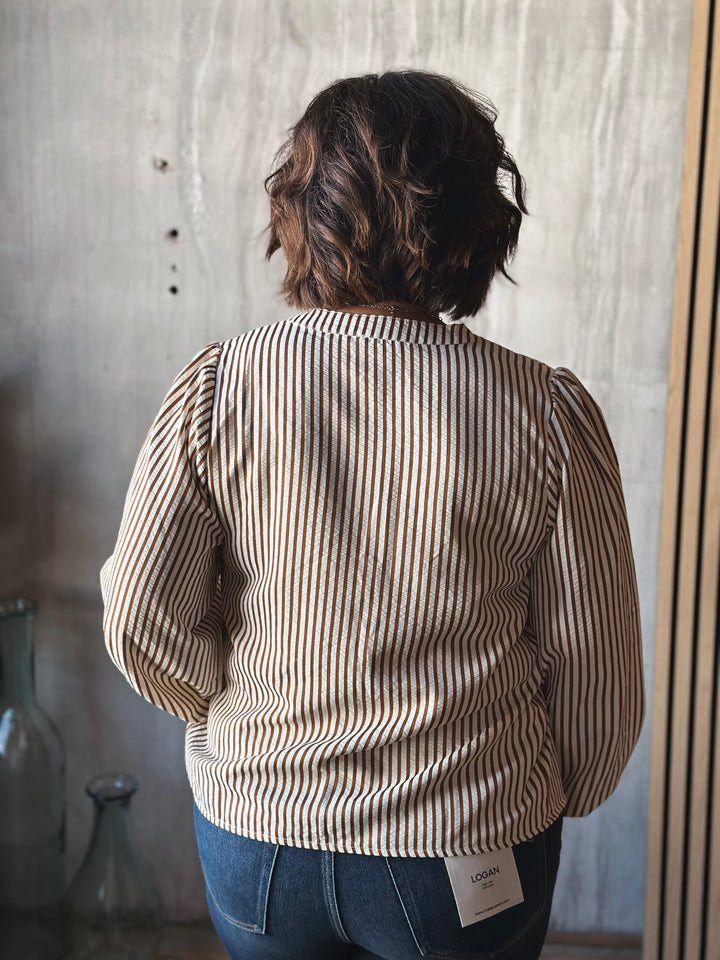 Person wearing a striped shirt with a visible brand tag, standing against a neutral wall.