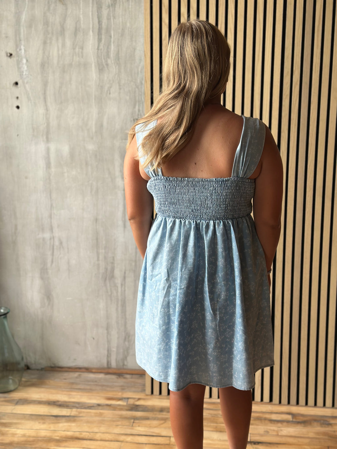 Woman wearing a light blue dress standing against a wooden wall.