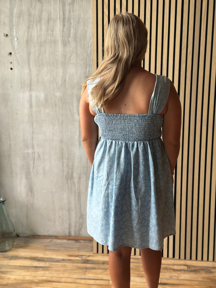 Woman wearing a light blue dress standing against a wooden wall.