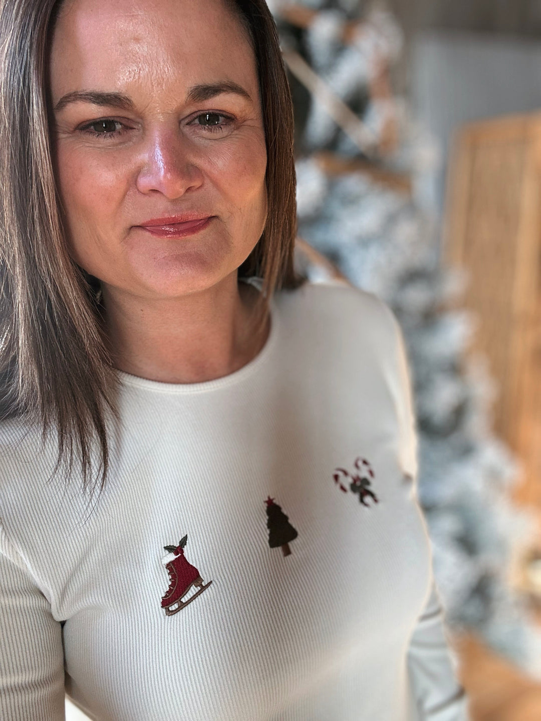 Woman wearing a white sweater with embroidered designs in a blurred indoor setting