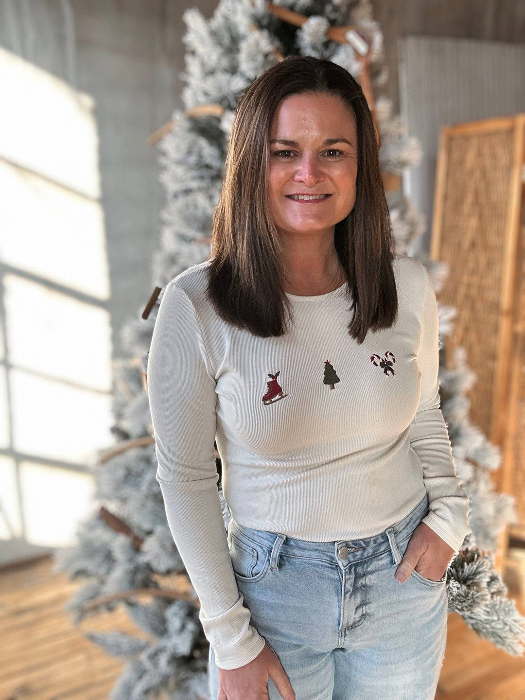 Woman wearing a cream sweater with tree designs in front of a decorated Christmas tree.