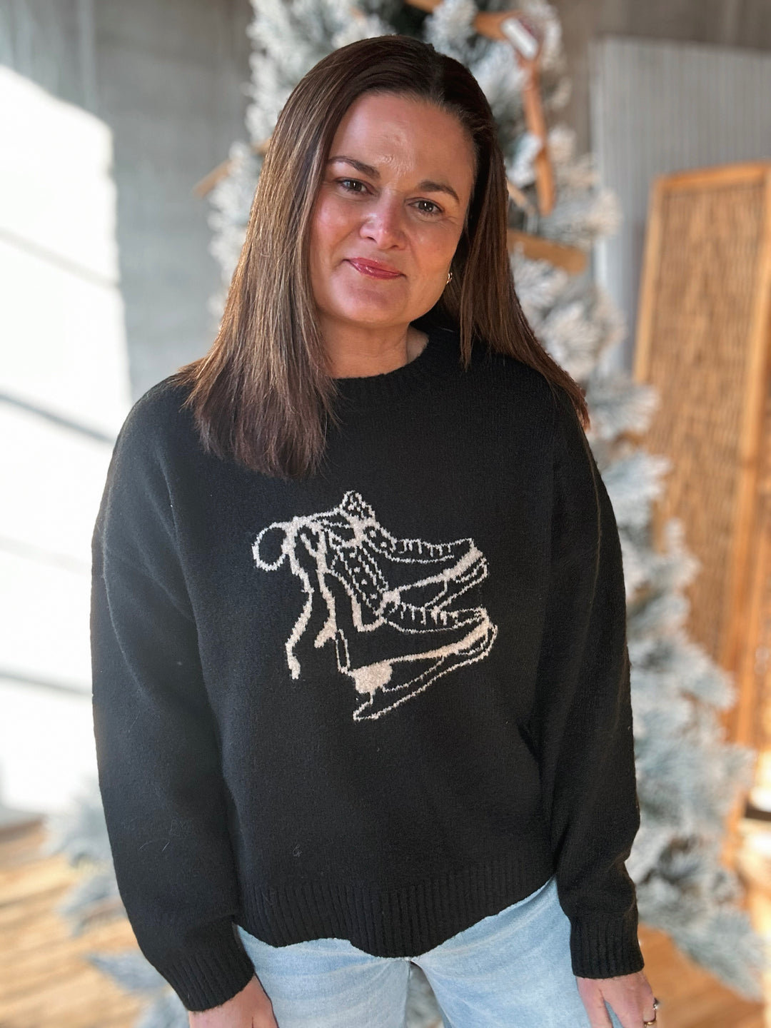 Woman wearing a black sweater with a white graphic design, standing indoors.