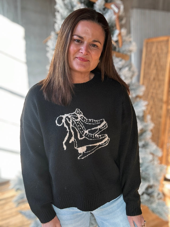 Woman wearing a black sweater with a white graphic design, standing indoors.