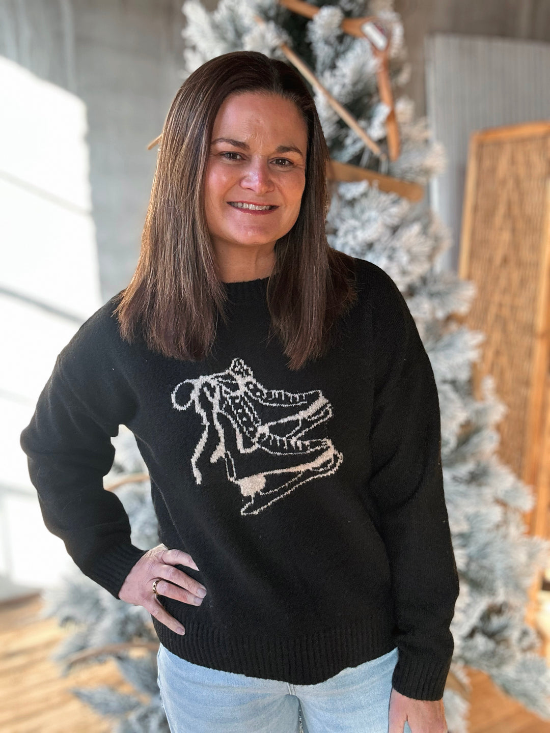 Person wearing a black sweater with a white graphic design, standing in front of a decorated Christmas tree.