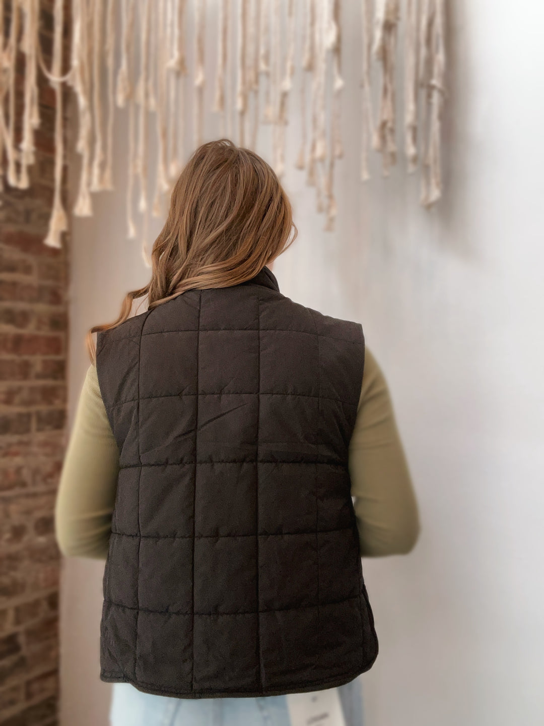 Person wearing a dark brown puffer vest standing in front of a wall with hanging ribbons.