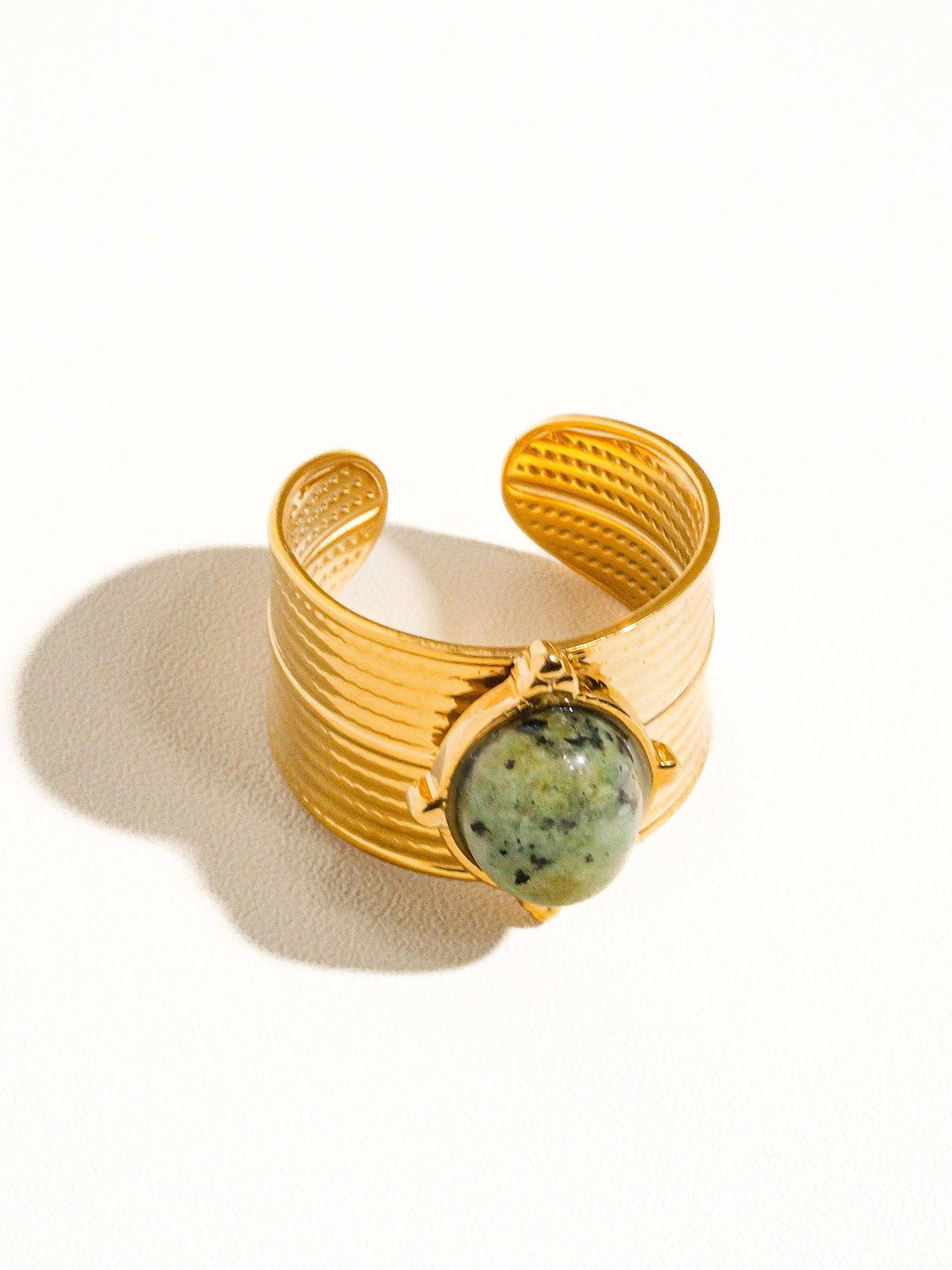 Gold cuff bracelet with a green stone on a white background