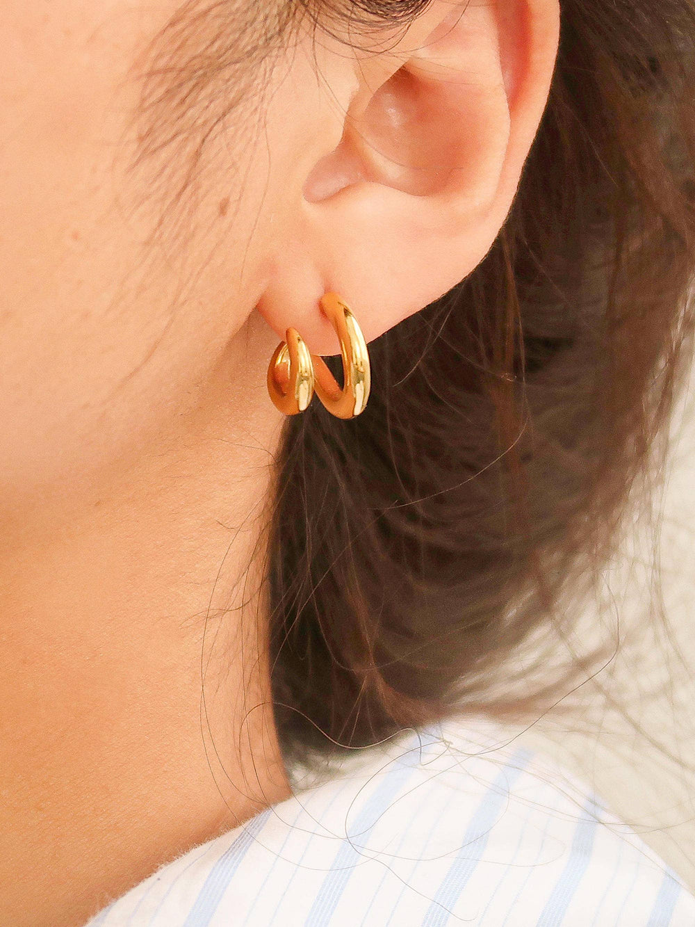 Gold hoop earrings worn by a person with dark hair.