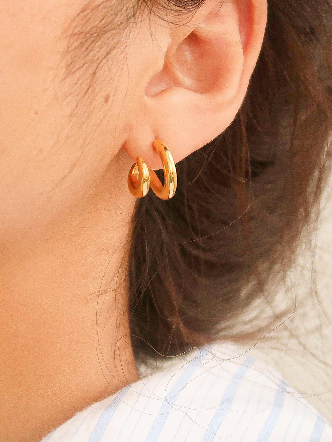 Gold hoop earrings worn by a person with dark hair.