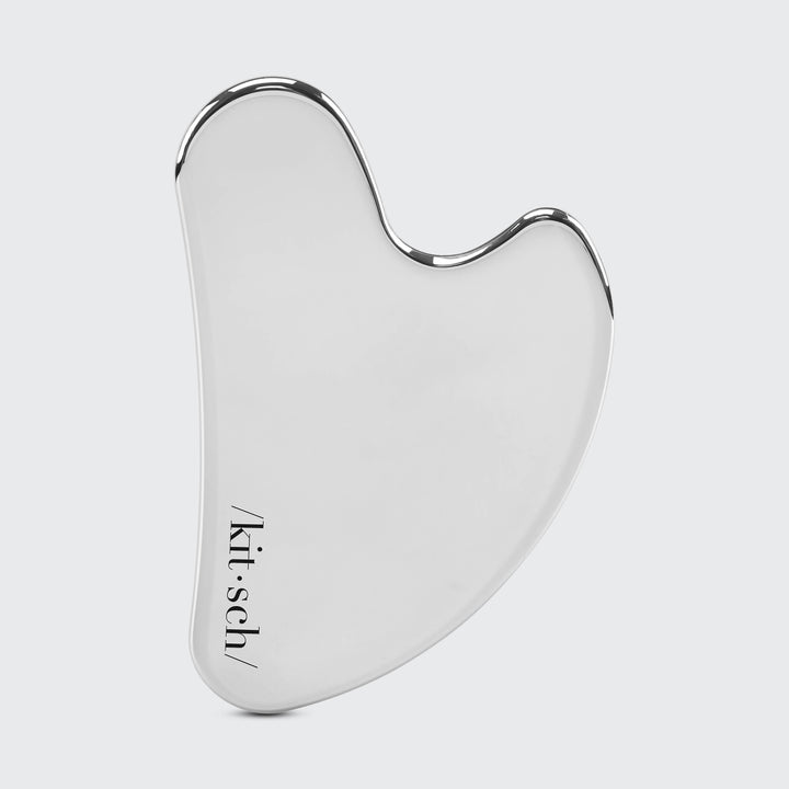Silver facial gua sha tool with 'kit-sch' branding on a light gray background