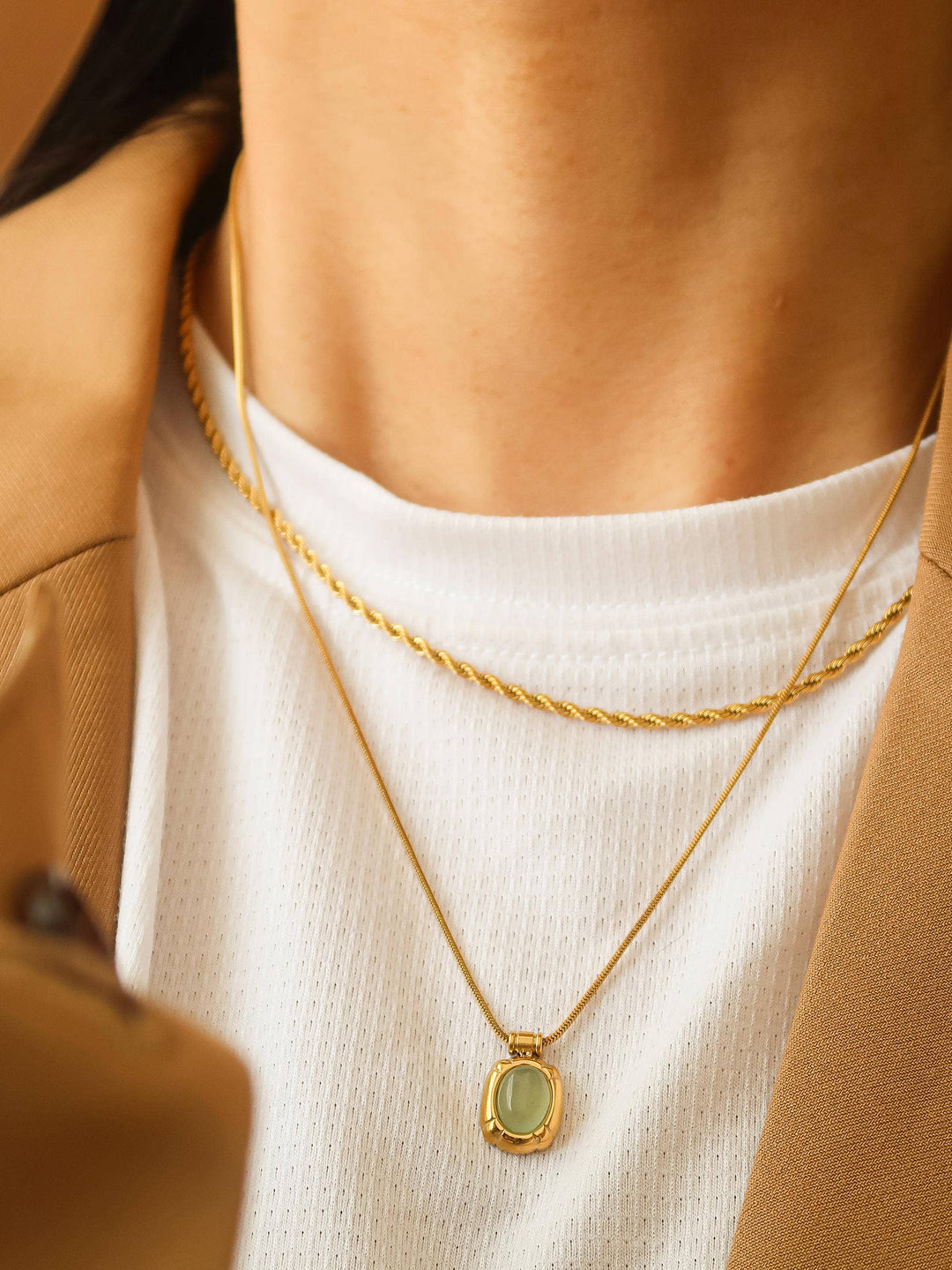 Close-up of a person wearing a gold necklace with a green pendant.