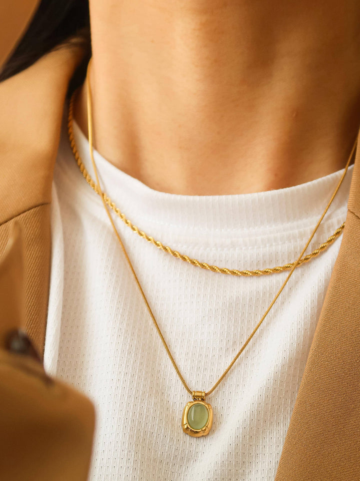 Close-up of a person wearing a gold necklace with a green pendant.