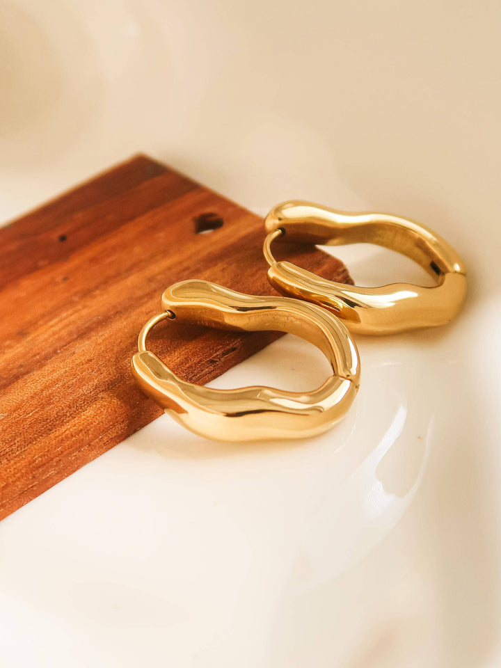 Gold hoop earrings on a wooden and white surface