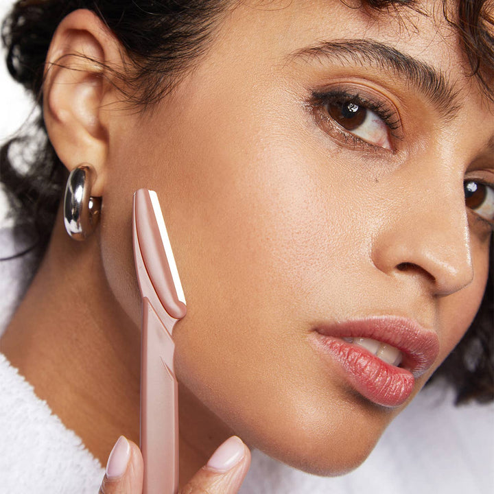 Close-up of a woman holding a pink makeup tool near her face