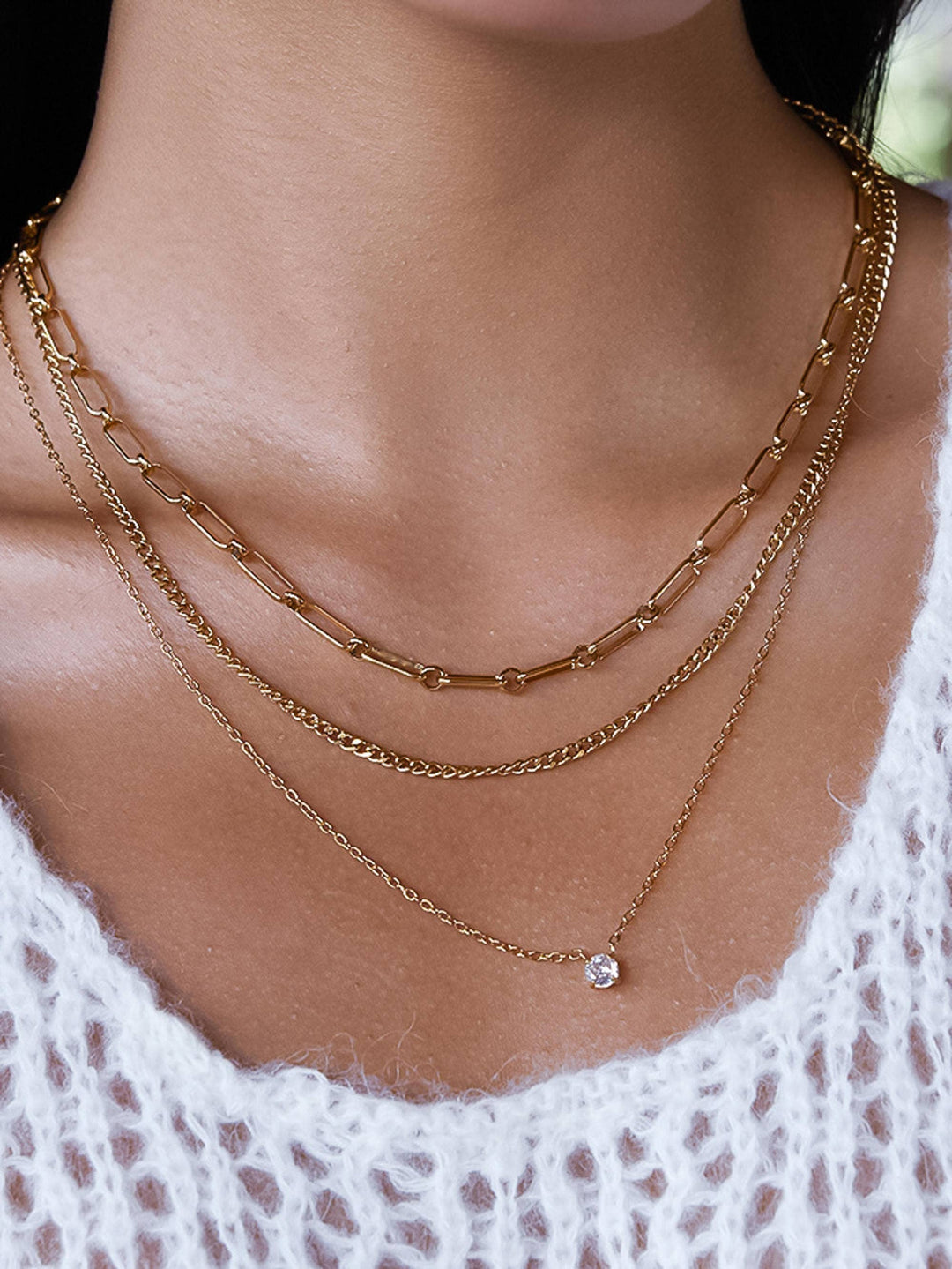 Close-up of a person wearing multiple gold necklaces with a white lace garment.