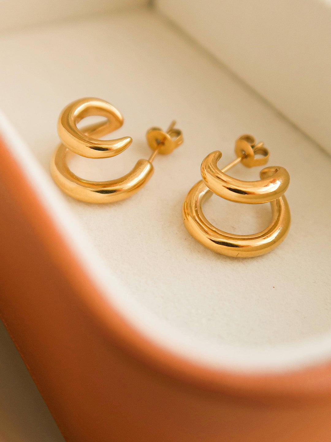 Gold hoop earrings on a white surface with a terracotta border