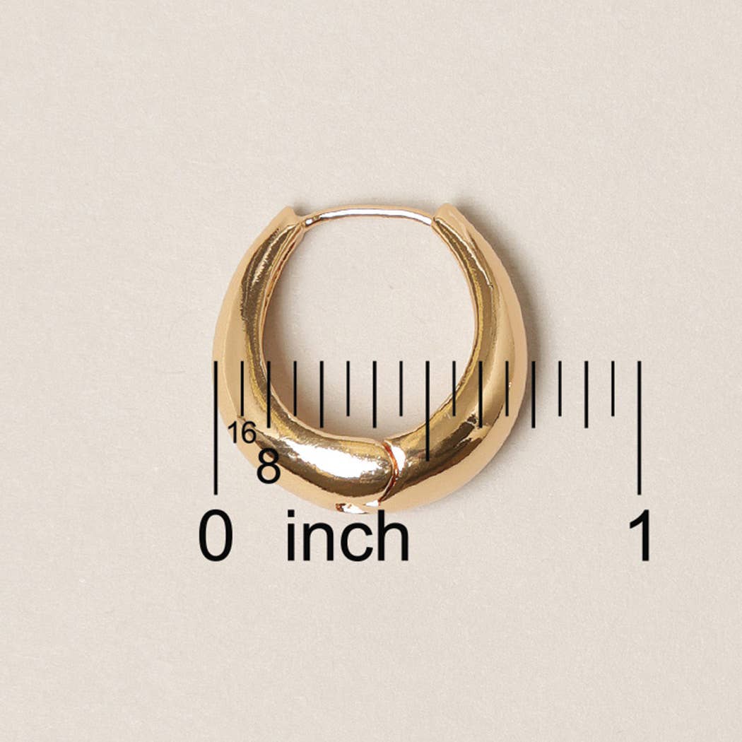 Gold hoop earring with a ruler for scale on a beige background