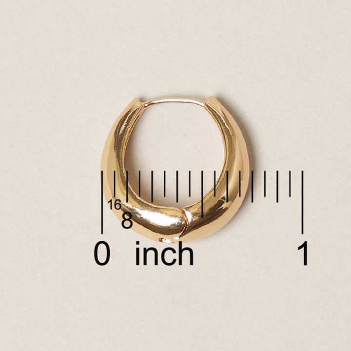Gold hoop earring with a ruler for scale on a beige background