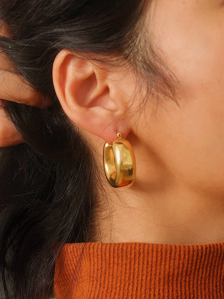 Close-up of a person wearing a gold hoop earring with a blurred background