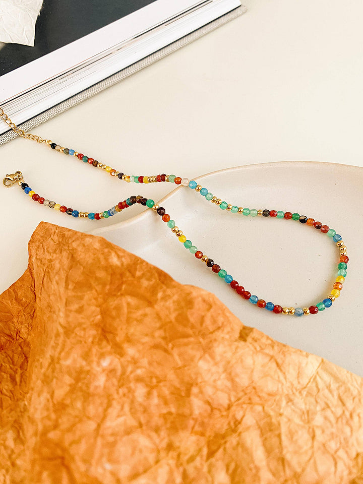 Colorful beaded necklace on a textured orange surface with a black and white striped background