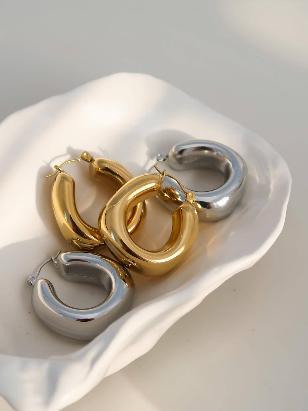 Three hoop earrings in gold, silver, and rose gold on a white shell.