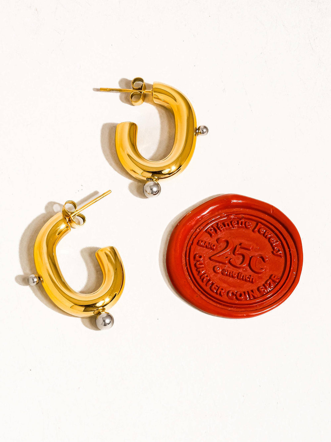 Gold hoop earrings with a red stamp-like design on a white background