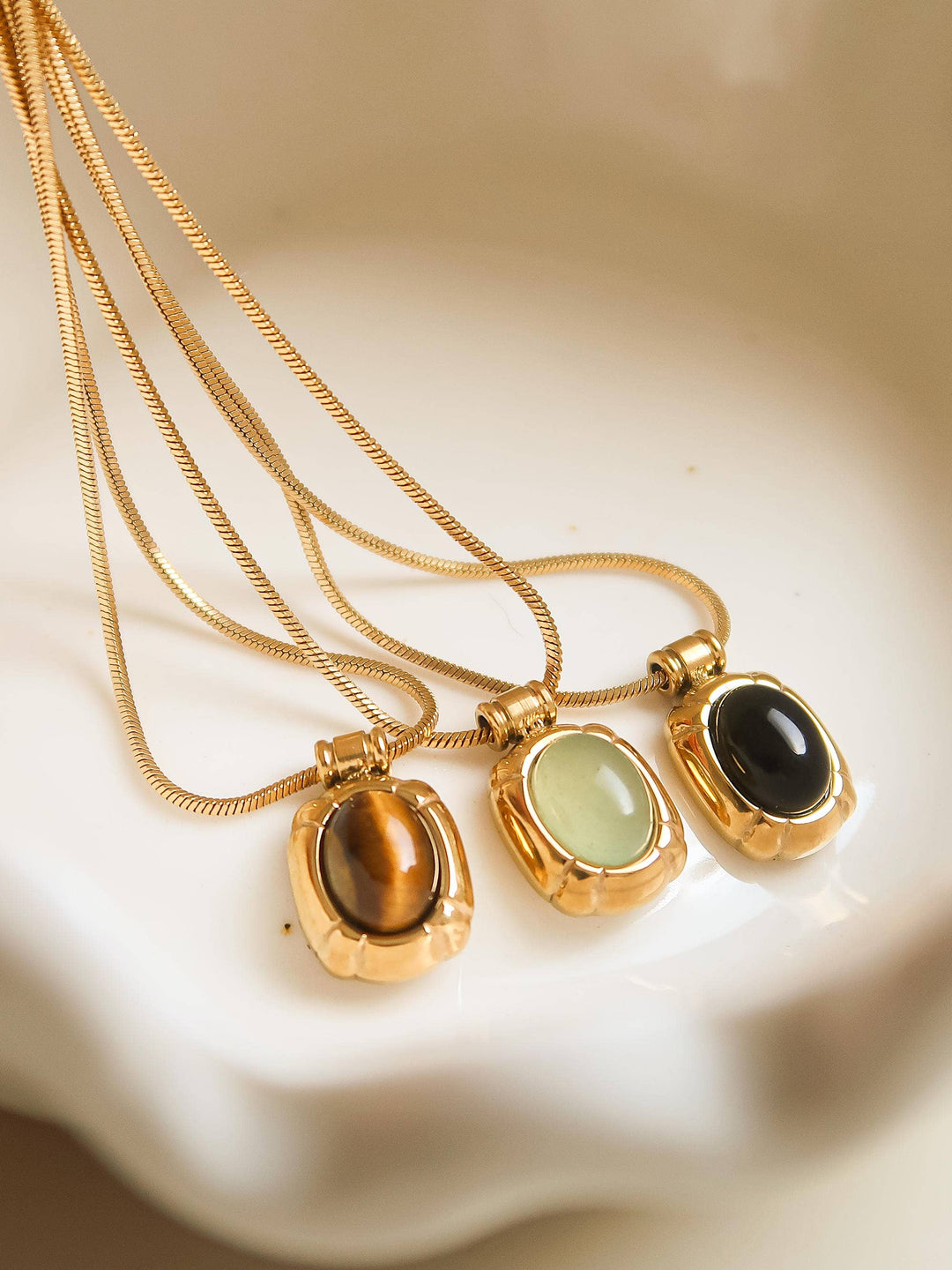 Three gold necklaces with different colored pendants on a beige surface