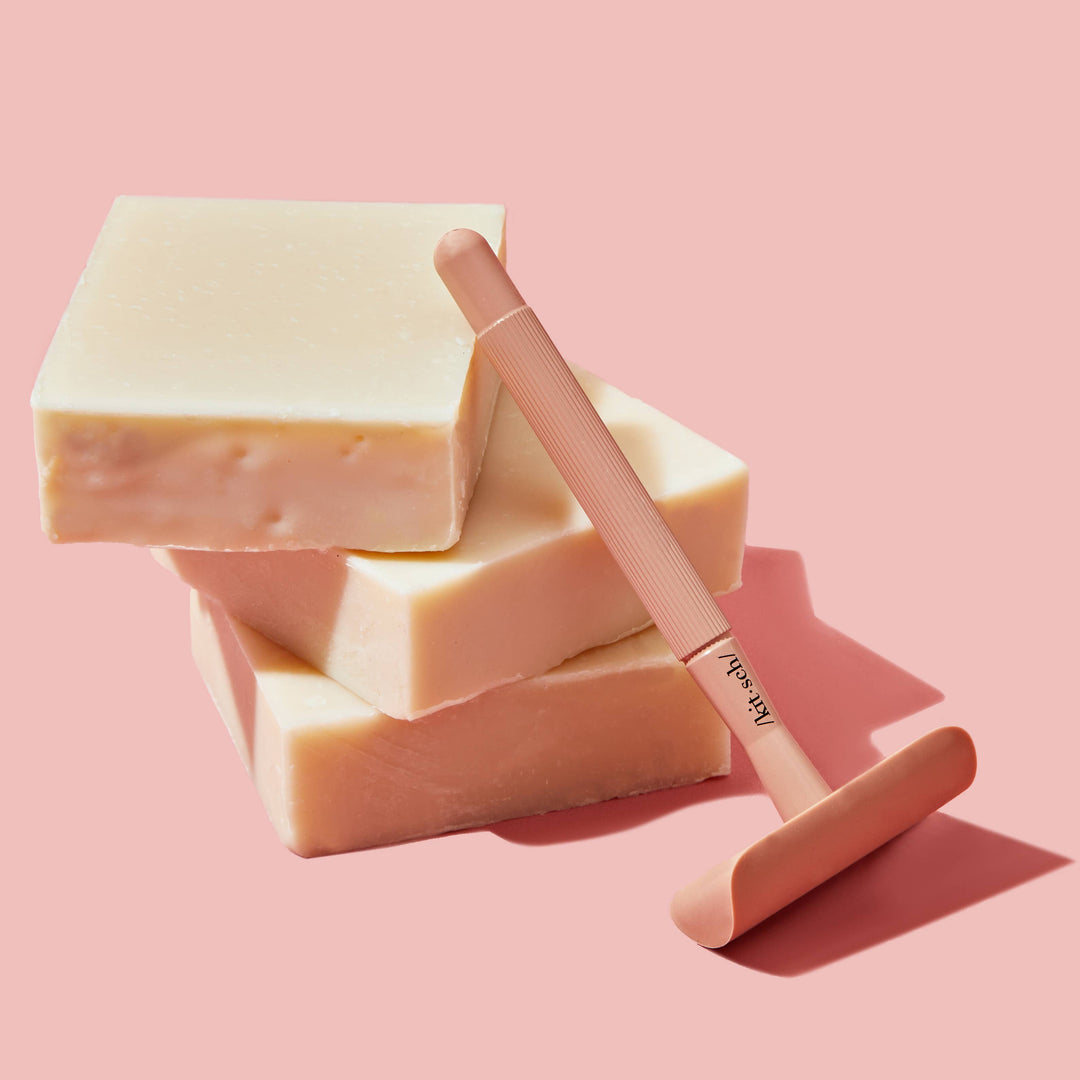 Three bars of soap and a pink safety razor on a pink background