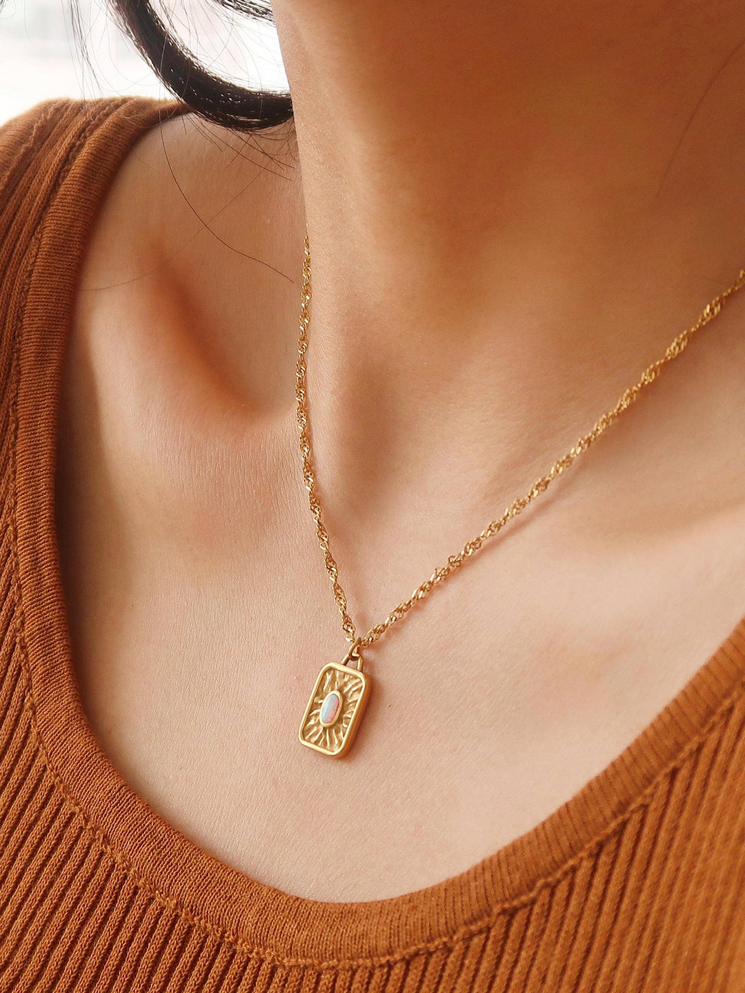 Gold necklace with a pendant on a person wearing a brown top