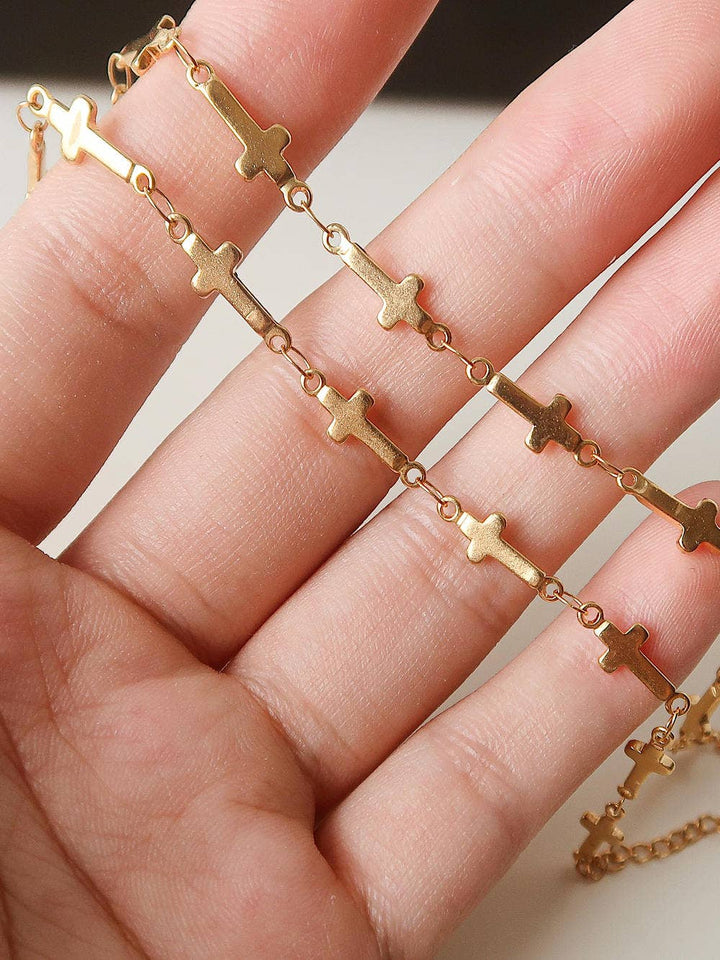 Gold chain bracelet with cross designs held on a hand against a neutral background